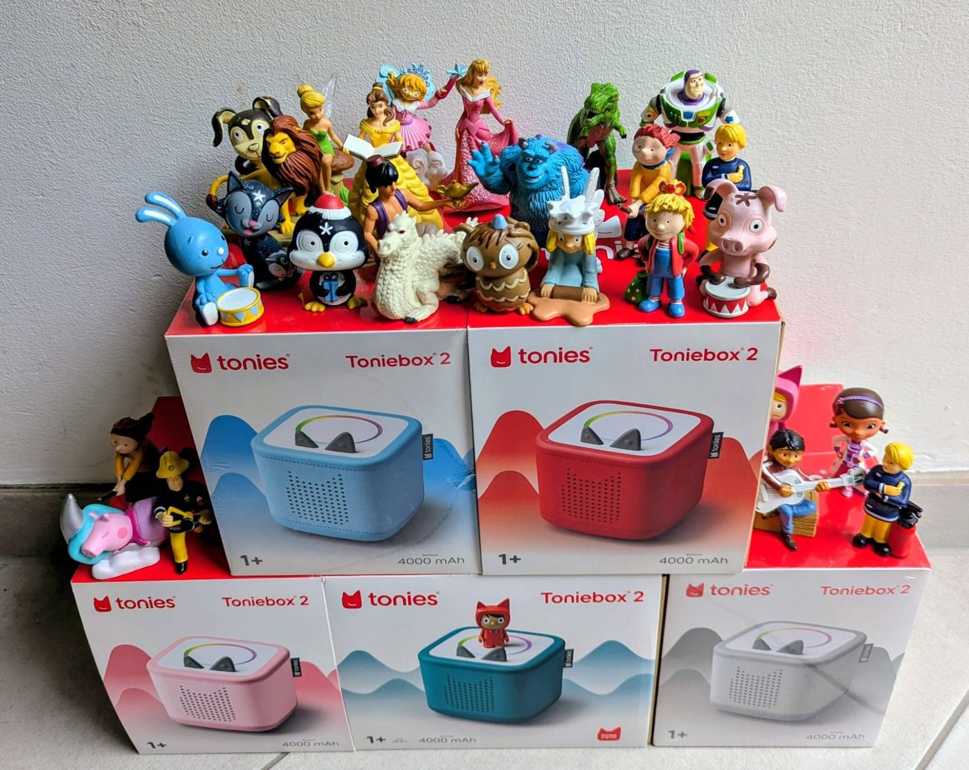Fünf Toniebox-2 in Blau, Rot, Rosa, Petrol und Grau, umringt von zahlreichen Toniefiguren